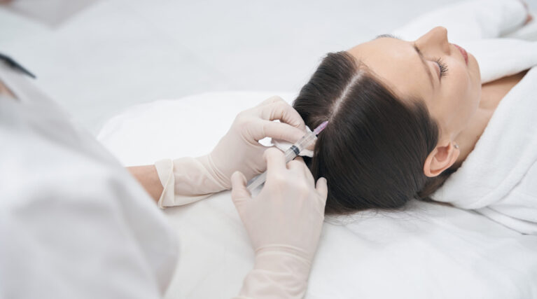 Woman receiving injection into scalp in beauty center Close up of doctor in sterile gloves doing mesotherapy injection into female head in cosmetology clinic