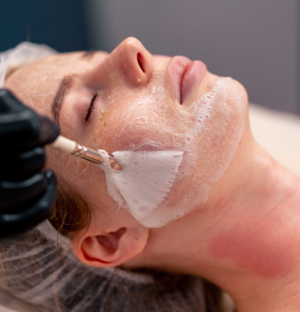 close-up beautician in gloves applies foam with a brush to the client's face takes care of skin
