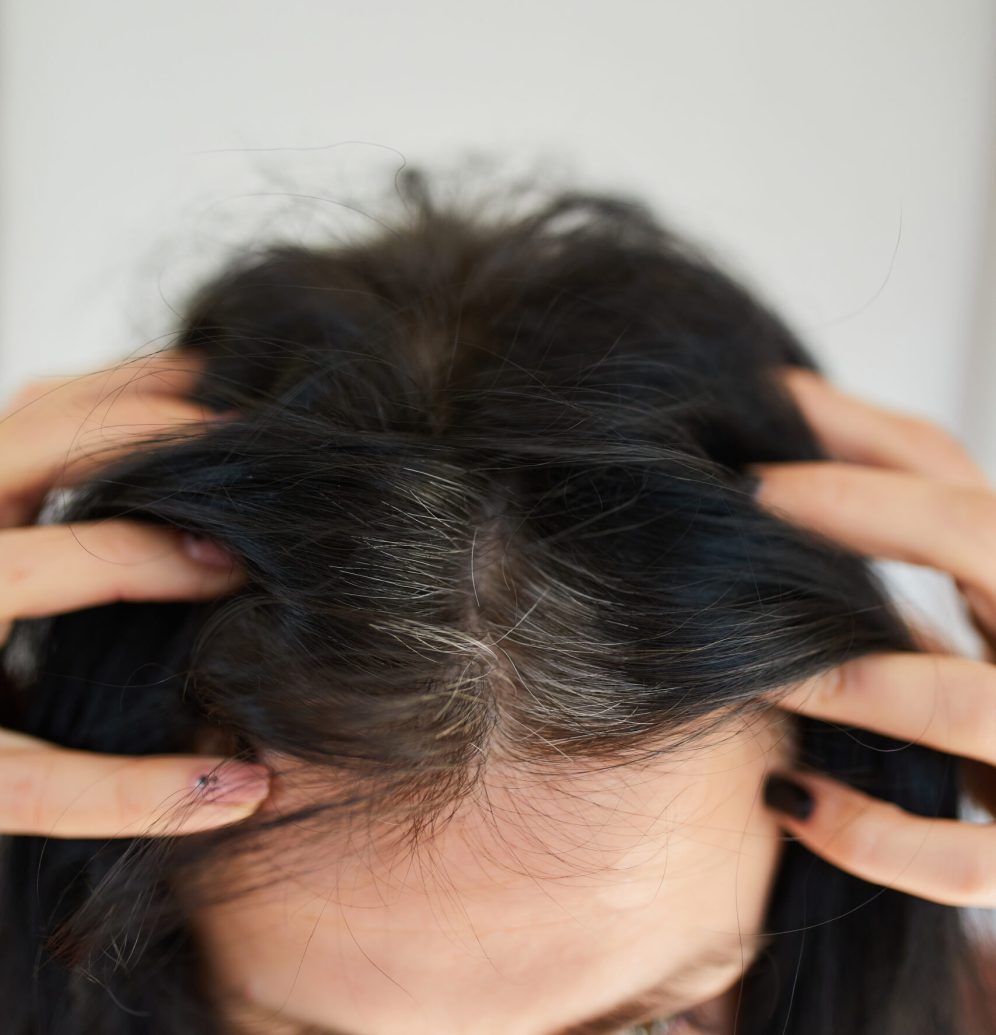 Portrait of a beautiful young woman examining her scalp and hair in mirror, hair roots, color, first grey hair, hair loss or dry scalp problem, or noticing that she is suffering from dandruff